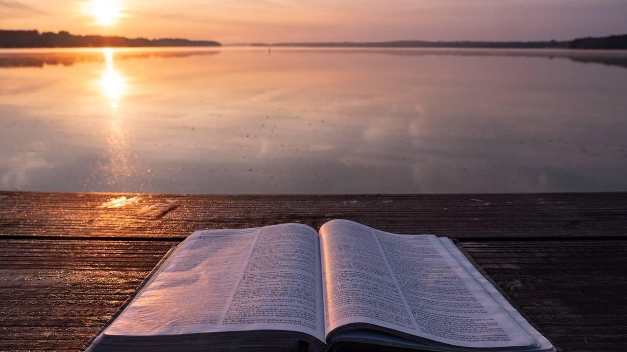 Open Bible resting on a wooden dock at sunrise, overlooking a still lake—symbolizing peace, reflection, and spiritual grounding.