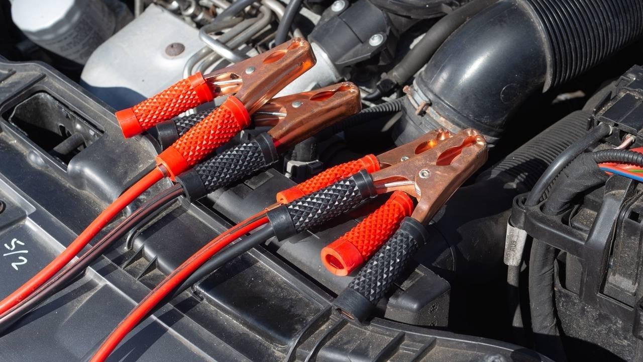 Close-up of red and black jumper cables connected to a car battery under the hood.